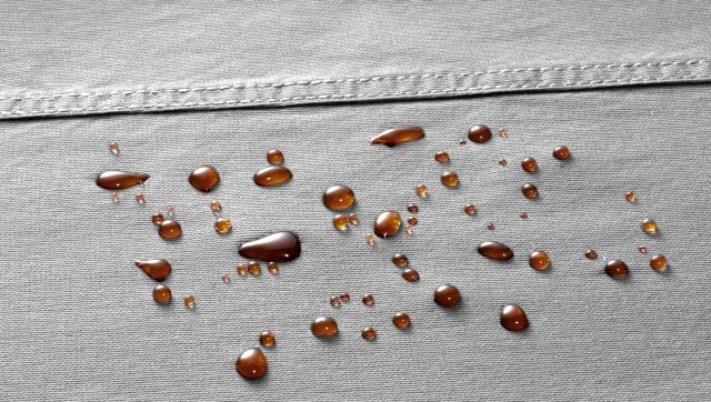 Nahaufnahme eines wasserabweisenden, grauen Stoffs mit braunen Tropfen.