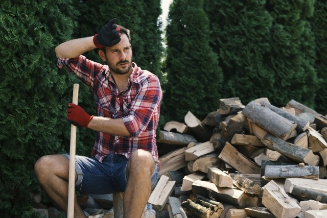Holzfäller sitzt im Wald und wischt sich den Schweiß von der Stirn