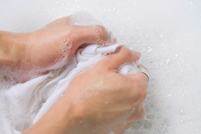 Zwei Hände, die einen Stoff mit der Hand waschen.