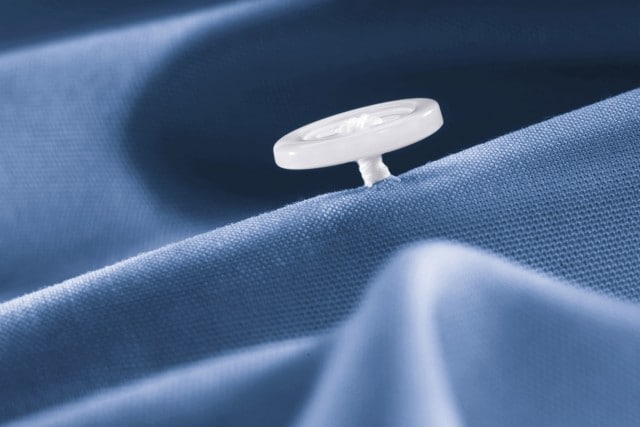 Detailaufnahme eines blauen Baumwollhemds mit einem weißen Knopf, der auf dem Stoff sichtbar ist.