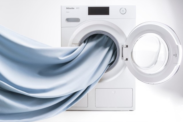 .Blaue Baumwollstoffe werden in einer geöffneten Waschmaschine gewaschen.