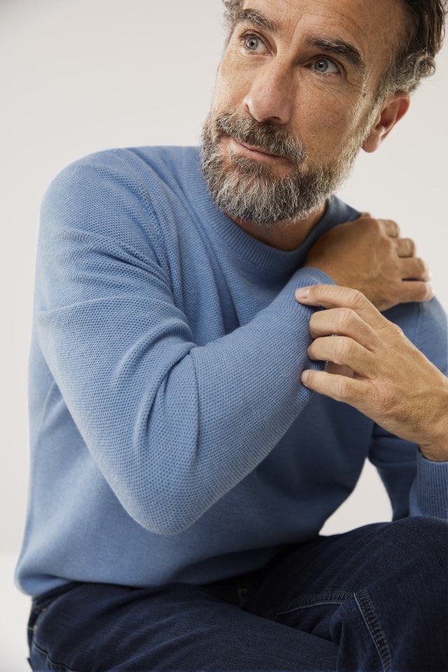 Mann in blauem Pullover sitzt und schaut zur Seite.