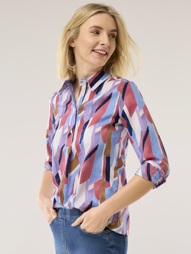 Eine Frau mit bunter Bluse und einer Jeans schaut zur Seite