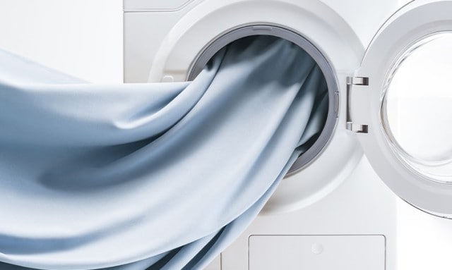 Ein hellblauer Stoff ragt aus der geöffneten Tür einer Waschmaschine.