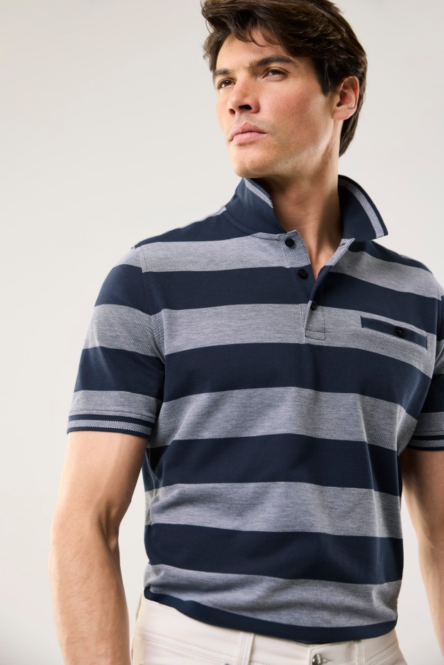 Ein Mann trägt ein kurzärmeliges Poloshirt mit breiten, waagerechten dunkelblauen und hellgrauen Streifen sowie eine helle Hose.
