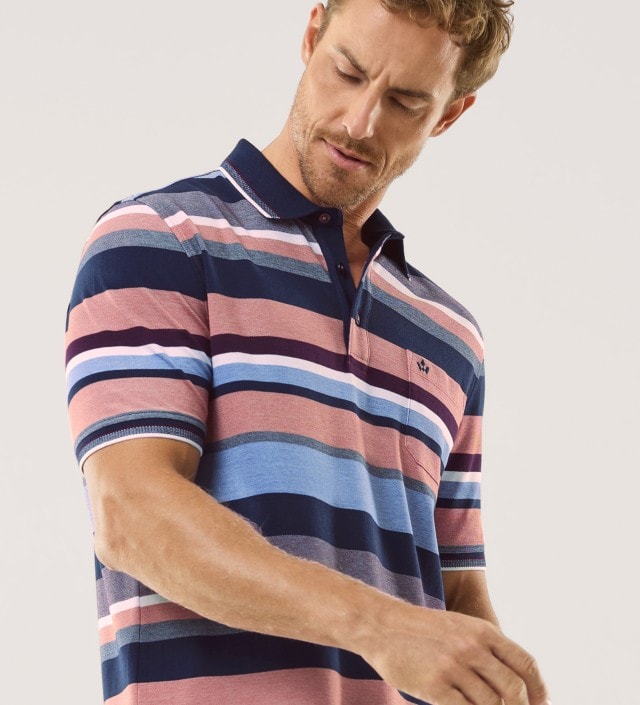 Ein Mann trägt ein gestreiftes Poloshirt in mehreren Farben und blickt nach unten.