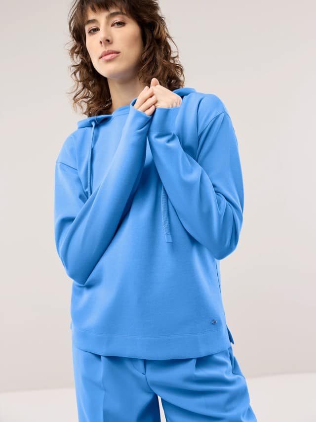 Eine Frau trägt ein blaues Hoodie‑Set, das sportlich, modern und ruhig‑lässig wirkt. Eine Frau trägt ein blaues Hoodie‑Set, das sportlich, modern und ruhig‑lässig wirkt.