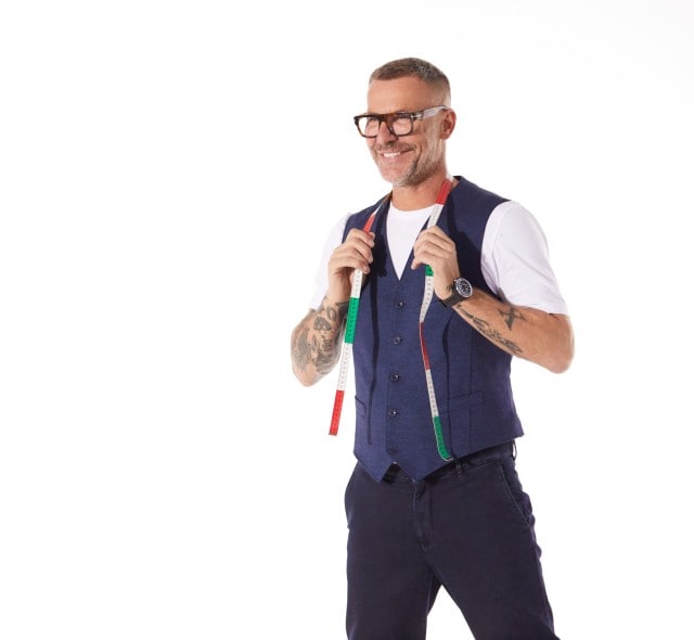 Mann mit Brille und Bart, trägt Weste und T-Shirt. Hält Maßband um den Nacken.