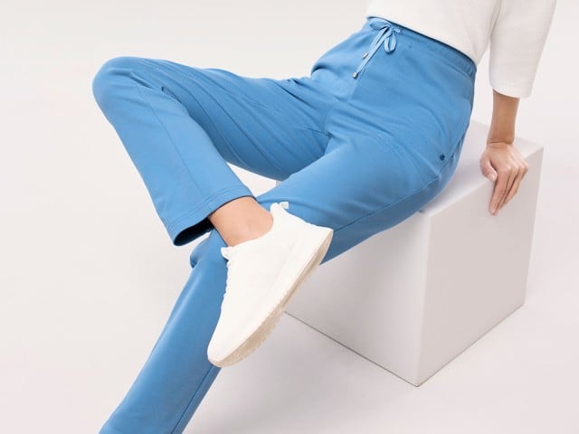 Eine Person sitzt auf einem weißen Block und trägt eine blaue Jogginghose, weiße Sneaker und ein helles Oberteil.