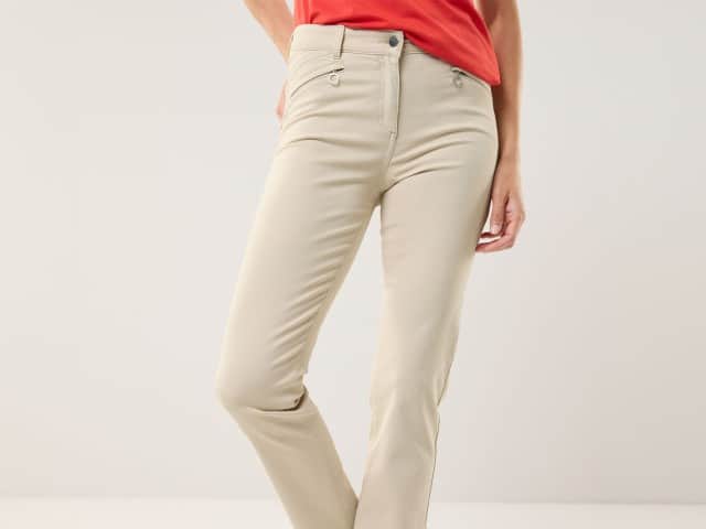 Eine Frau trägt eine beigefarbene Hose mit geradem Schnitt und ein rotes Oberteil.