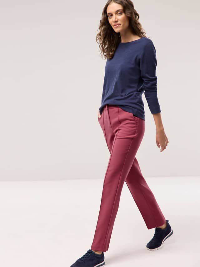 Eine Frau geht locker dahin und trägt ein dunkelblaues Langarmshirt, eine pinkrote Hose und dunkle Sneakers.