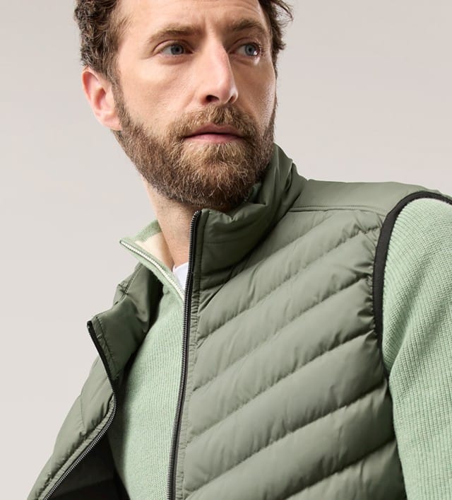 Eine Frau trägt eine gesteppte Jacke mit Kapuze in Beige und ein Mann trägt eine grüne Steppweste mit passendem Oberteil.