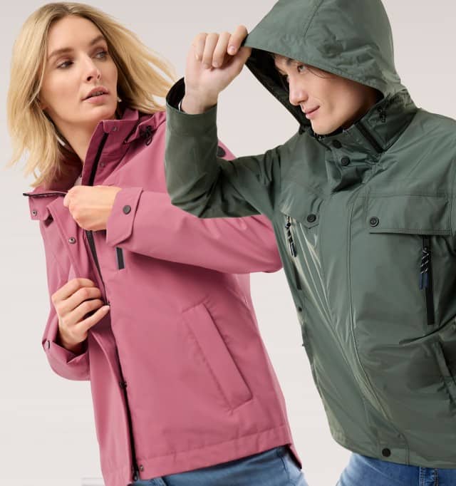 Ein Frau trägt eine Aquastop Jacke in Rosenholz, ein Mann daneben in der Aquastop Reisejacke in Salbei.