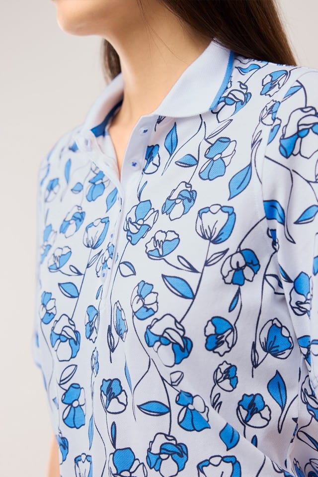 Eine Frau trägt ein Extraglatt Polo mit Blumen in Meerblau.