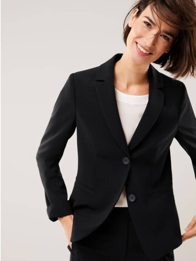 Eine Frau trägt einen schwarzen Blazer über einem weißen Oberteil.