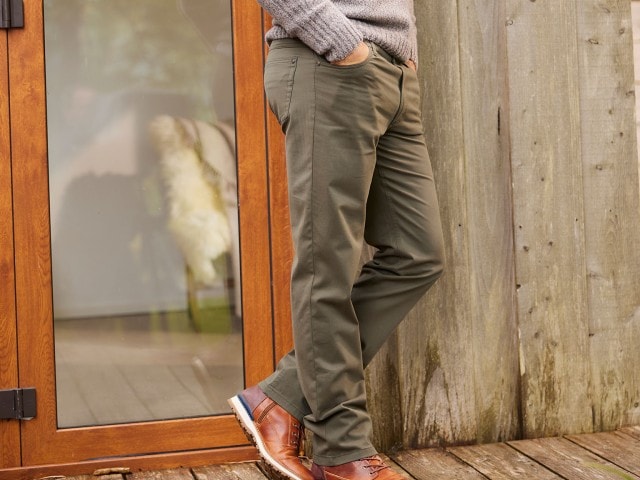 Mann trägt eine dunkelgrüne five Pocket Jeans und lehnt sich an eine Wand an