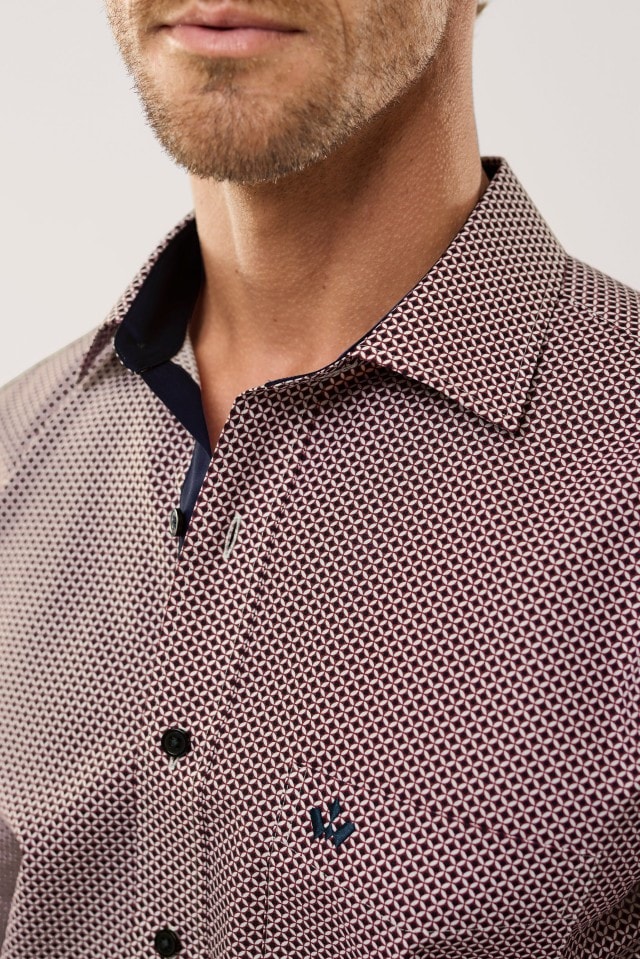 Eine Person trägt ein Hemd mit kleingemustertem, geometrischem Muster in Rot und Weiß sowie dunklen Knöpfen.