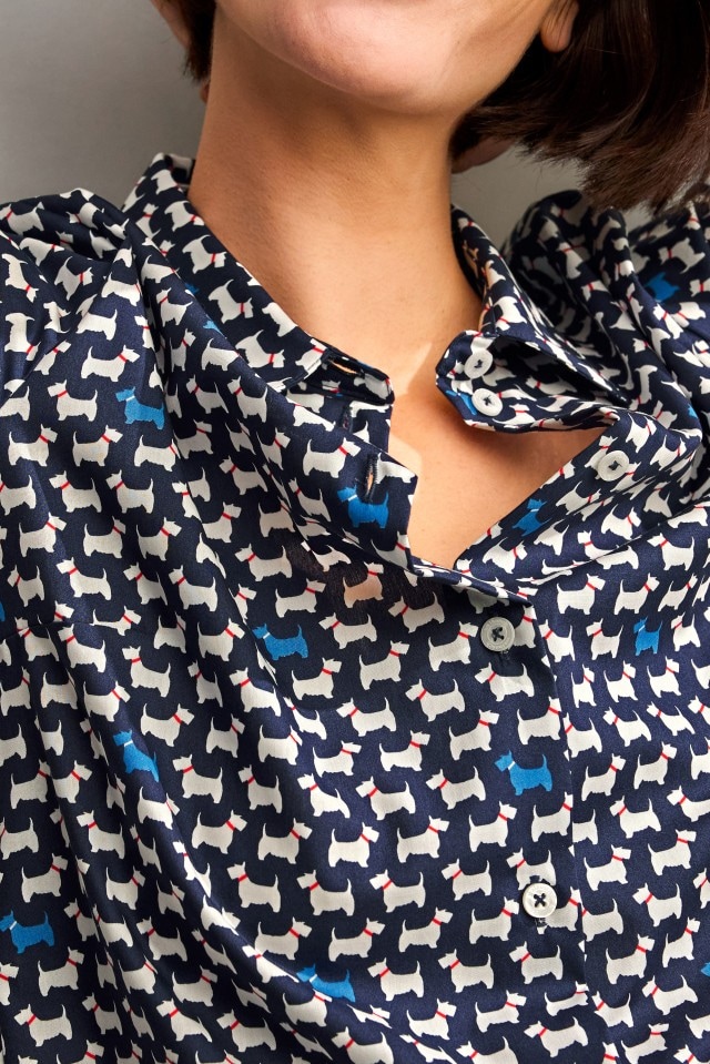 Eine Person trägt eine dunkelblaue Bluse mit einem Muster aus weißen und vereinzelten blauen Hunden mit roten Halsbändern.