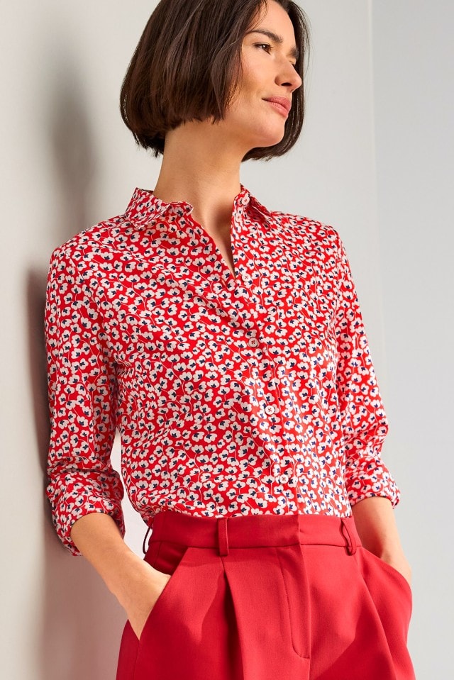 Eine Person trägt eine rote Bluse mit weiß-blauem Blumenmuster, kombiniert mit einer roten Hose.