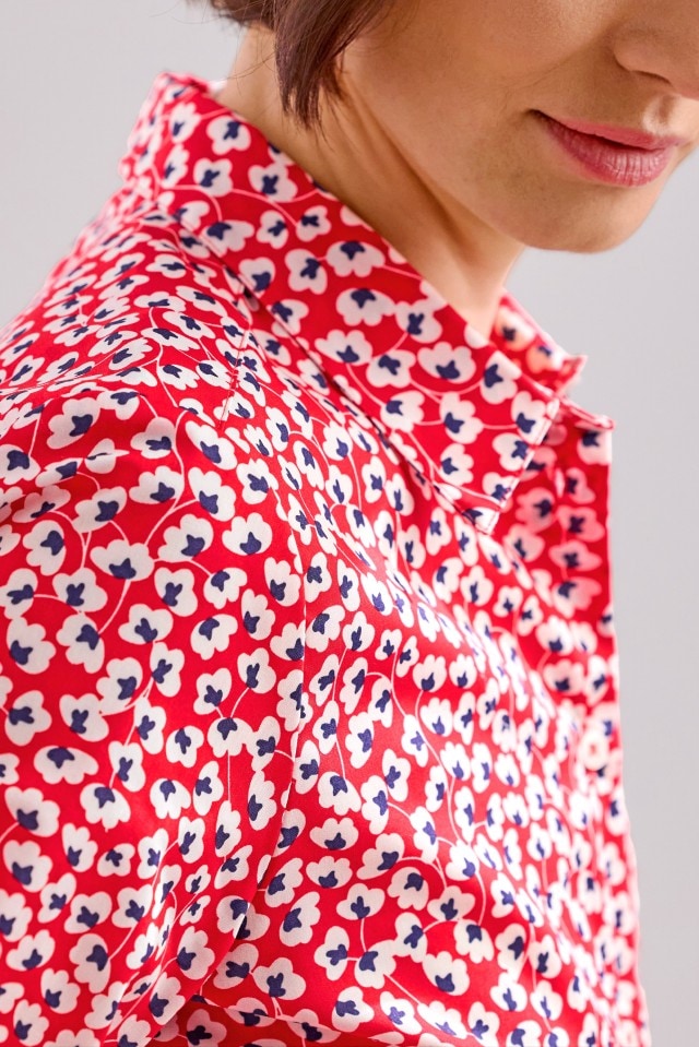 Eine Person trägt eine rote Bluse mit einem Muster aus weißen und blauen Blumen.