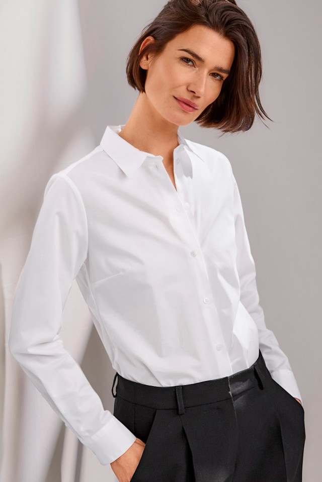 Eine Person trägt eine klassische weiße Bluse mit langen Ärmeln, kombiniert mit einer schwarzen Hose.