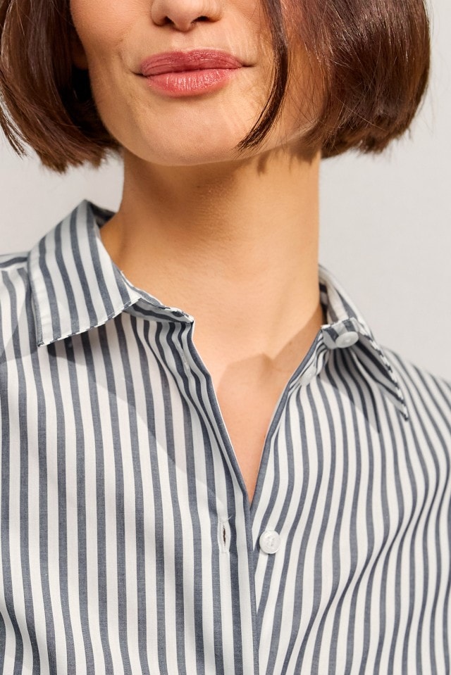Eine Person trägt eine weiß-blau gestreifte Bluse mit klassischem Kragen und weißen Knöpfen.