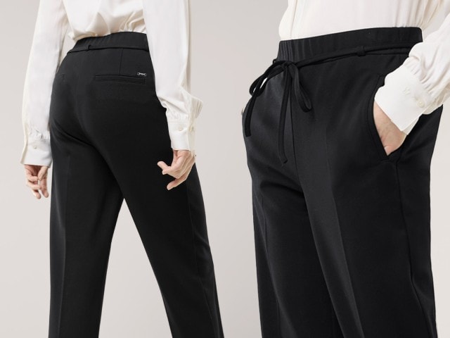 Eine Frau trägt eine elegante schwarze Stoffhose mit Bindegürtel und kombiniert dazu eine weiße Bluse. Der Look wirkt klassisch und zugleich modern-schlicht.