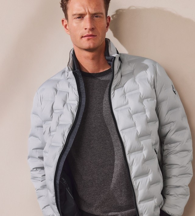 Ein Mann trägt eine hellgraue Steppjacke über einem dunkelgrauen Strickpullover. Der Look ist sportlich und zugleich lässig.