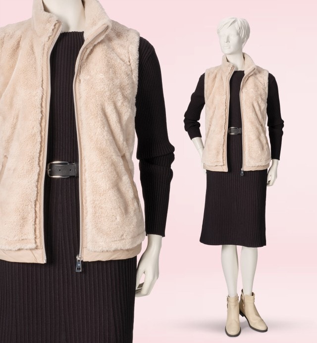 Eine Schaufensterpuppe trägt ein schwarzes Strickkleid mit Gürtel und einer hellen Kunstfellweste. Helle Stiefeletten runden den modernen, gemütlichen Look ab.