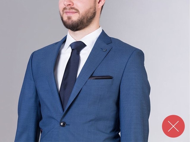 Mann trägt einen blauen Anzug, mit einer blauen Krawatte und einem weißen Hemd.