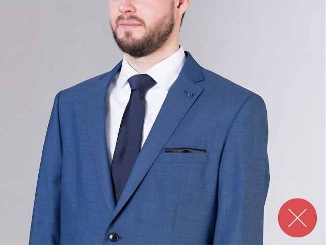 Mann trägt einen blauen Anzug, mit einer blauen Krawatte und einem weißen Hemd.
