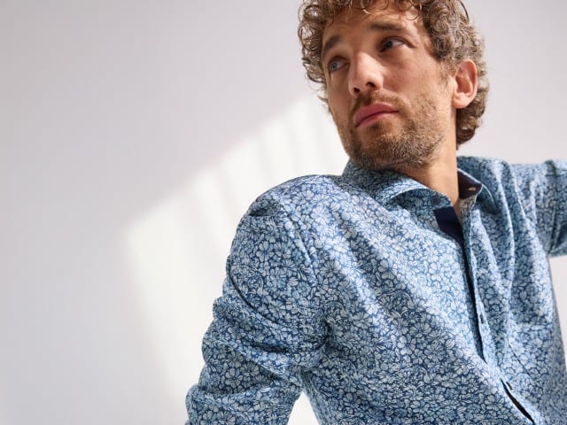 Ein Mann trägt ein geblümtes Hemd in Hellblau/Weiß.