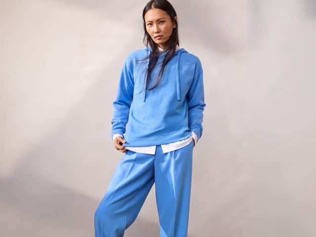 Eine Frau trägt einen hellblauen Hoodie über einer weißen Bluse und eine dazu passende hellblaue Hose. Eine Frau trägt einen hellblauen Hoodie über einer weißen Bluse und eine dazu passende hellblaue Hose.