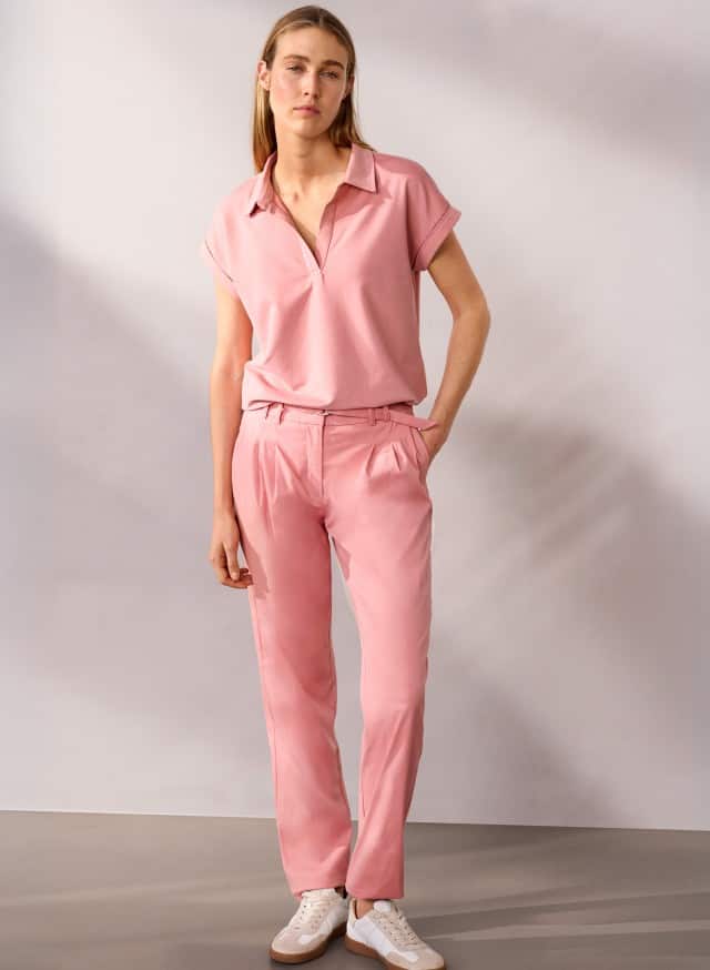 Eine Person steht vor einer neutralen Wand und trägt ein rosafarbenes Oberteil, eine passende rosafarbene Hose und weiße Sneaker. Eine Person steht vor einer neutralen Wand und trägt ein rosafarbenes Oberteil, eine passende rosafarbene Hose und weiße Sneaker.