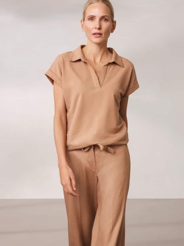 Eine Frau trägt ein beigefarbenes, locker fallendes Set aus Oberteil und Hose, das ruhig, weich und natürlich‑entspannt wirkt. Eine Frau trägt ein beigefarbenes, locker fallendes Set aus Oberteil und Hose, das ruhig, weich und natürlich‑entspannt wirkt.