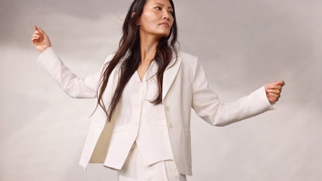 Eine Person trägt einen weißen Anzug mit Jacke, Weste und passender Hose und breitet leicht die Arme aus, während sie zur Seite blickt. Eine Person trägt einen weißen Anzug mit Jacke, Weste und passender Hose und breitet leicht die Arme aus, während sie zur Seite blickt.