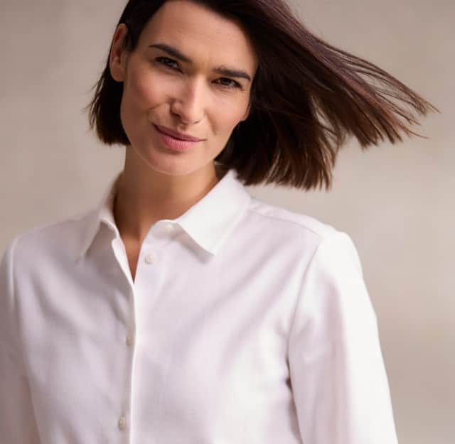 Eine dunkelhaarige Frau trägt eine weiße Bluse.