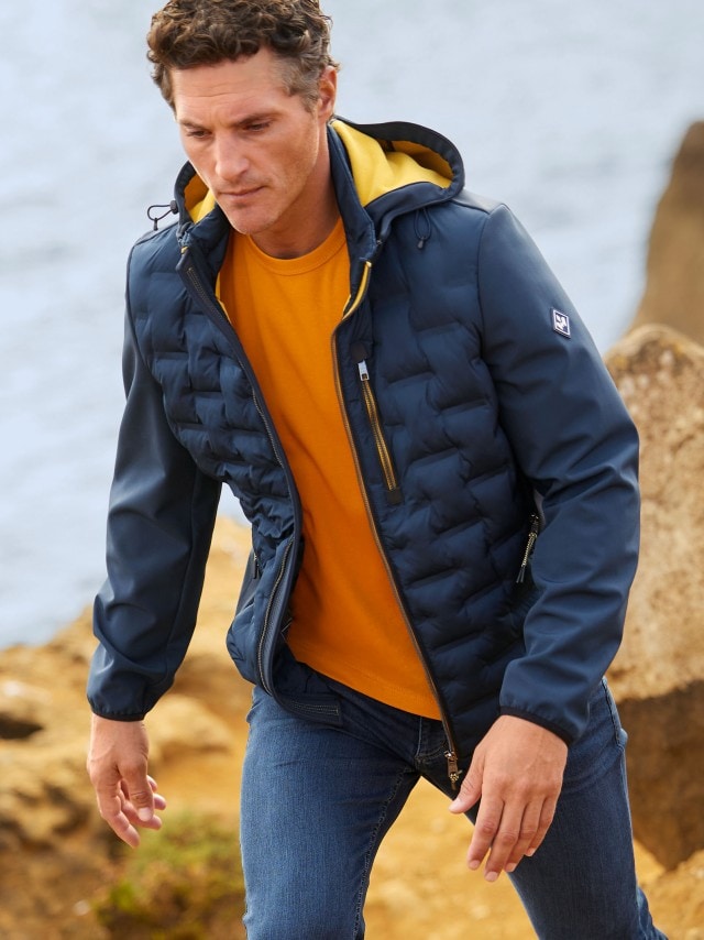 Ein Mann trägt eine Blouson und wandert an der Küste