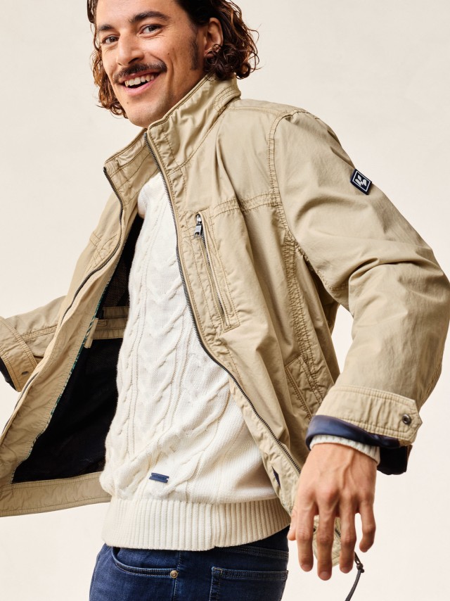 Ein Mann trägt ein Blouson in der Farbe sand, darunter einen Strickpullover.