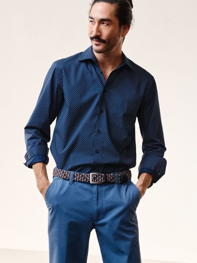 Ein Mann trägt ein gemustertes Hemd in Marine und hat seine Hände in den Taschen einer Chino. 