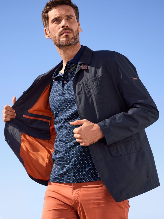 Dunkelhaariger Mann in blauem Aktiv-Sakko und Polo-Shirt in schwungvoller Pose.