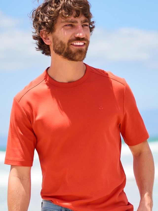 Mann trägt ein rotes T-Shirt und steht am Strand