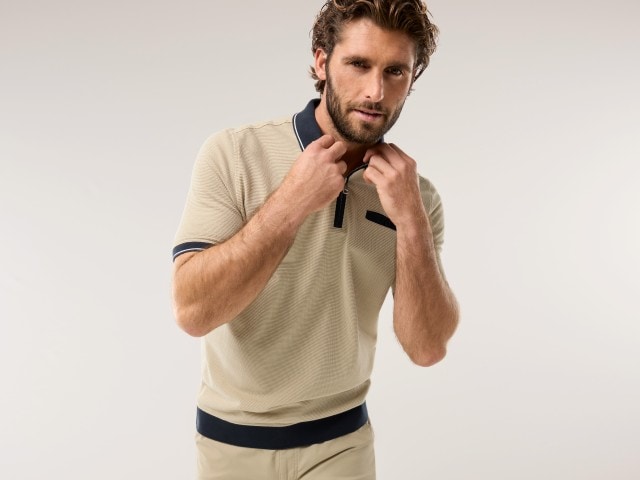 Mann trägt ein Poloshirt in beige und hält den Kragen mit seinen Händen hoch.