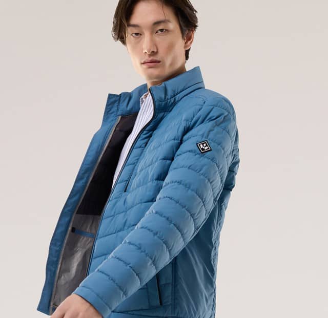 Ein Mann trägt eine gesteppte Jacke in Blau, darunter ein gestreiftes Hemd.