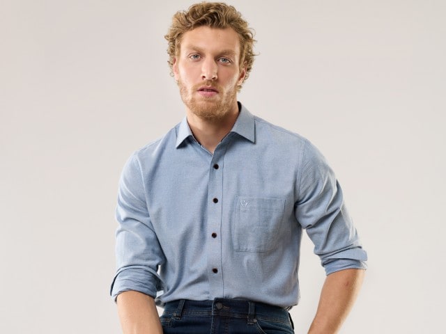 Ein Mann trägt ein hellblaues Hemd mit Brusttasche und hochgekrempelten Ärmeln zu einer Jeans.