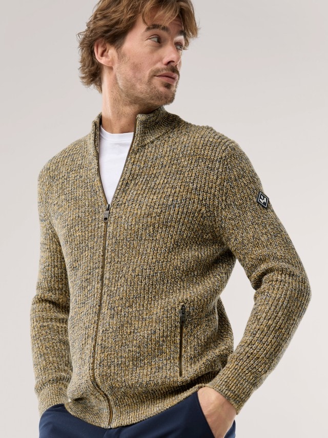Ein Mann trägt eine grob gestrickte, zweifarbige Strickjacke mit Reißverschluss und hohem Kragen.