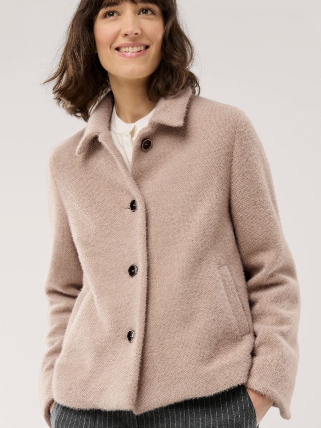 Eine Frau trägt eine beige, wollige Jacke mit Knopfleiste und Kragen.