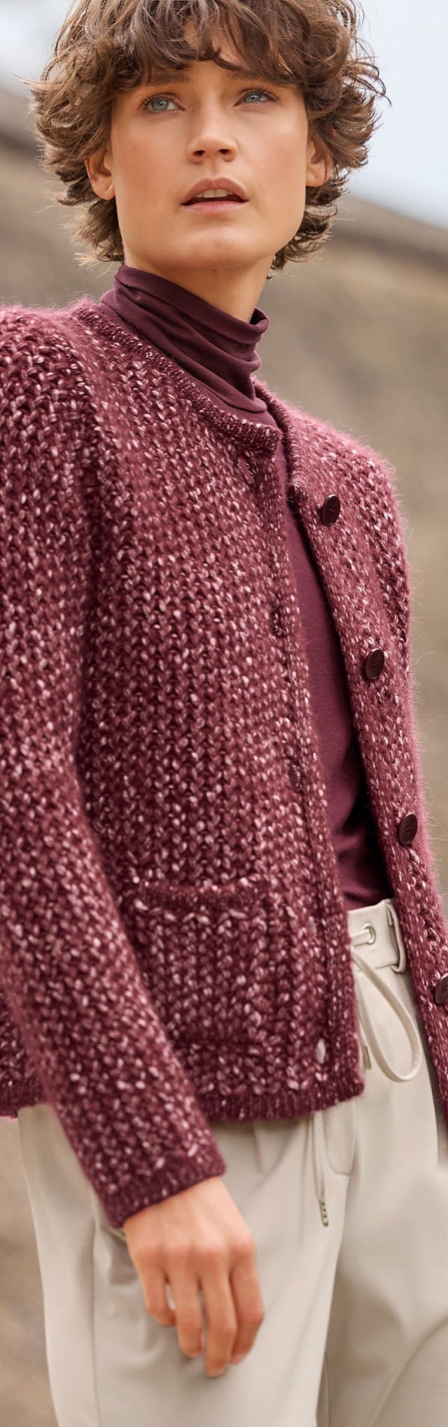 Eine Person trägt eine weinrote Strickjacke über einem Rollkragenpullover. Der Look wirkt warm, gemütlich und elegant.