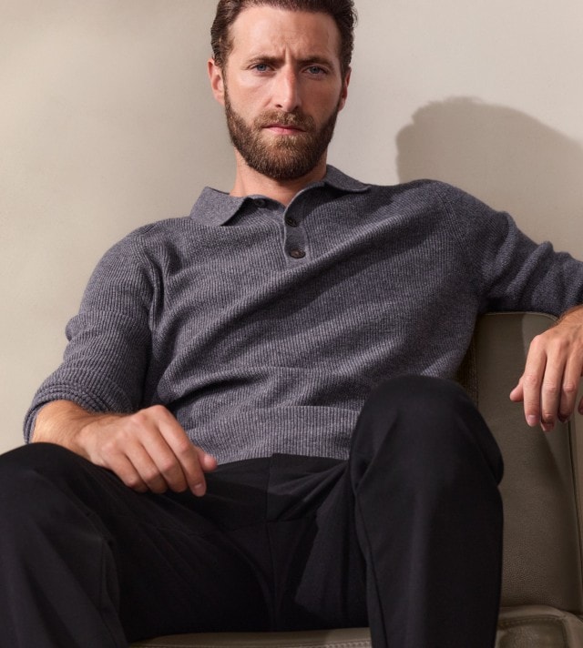 Ein Mann trägt einen grauen Strickpullover mit Knopfleiste und eine schwarze Hose. Der Look wirkt lässig-elegant und gleichzeitig schlicht.