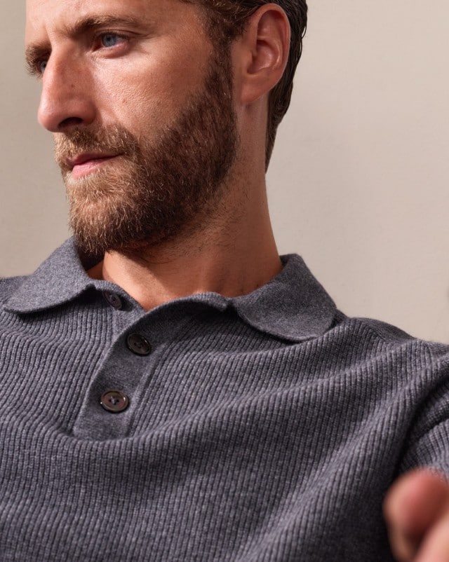 Ein Mann trägt einen grauen Strickpullover mit Knopfleiste und eine schwarze Hose. Der Look wirkt lässig-elegant und gleichzeitig schlicht.